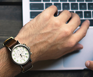 Man's hand in cool watch above macbook touch bar