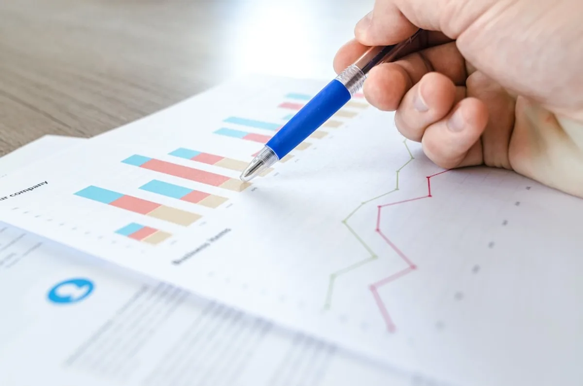 Hand with pen pointing at a paper with bar and line charts, analyzing targeted mail marketing campaign success.