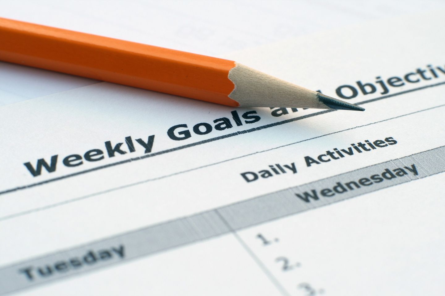 A close-up of an orange pencil resting on a “Weekly Goals and Objectives” sheet, symbolizing the strategic planning and setting of effective Email Marketing Objectives for successful campaigns.