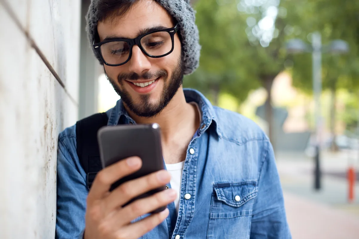 Young man smiling while viewing a mobile-optimized B2B email on his smartphone outdoors, demonstrating responsive design and user-friendly interface.