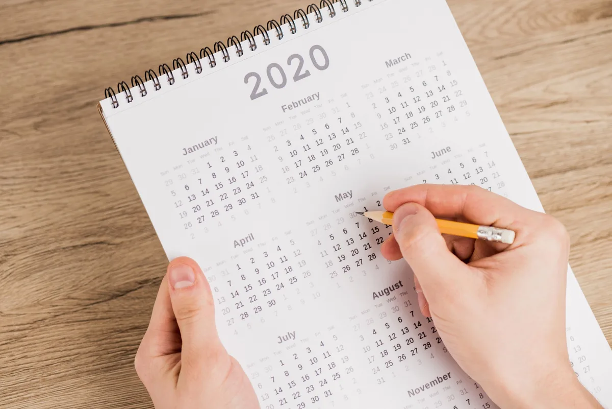 Hand holding a calendar and marking a date, symbolizing planning the best time to send marketing emails.