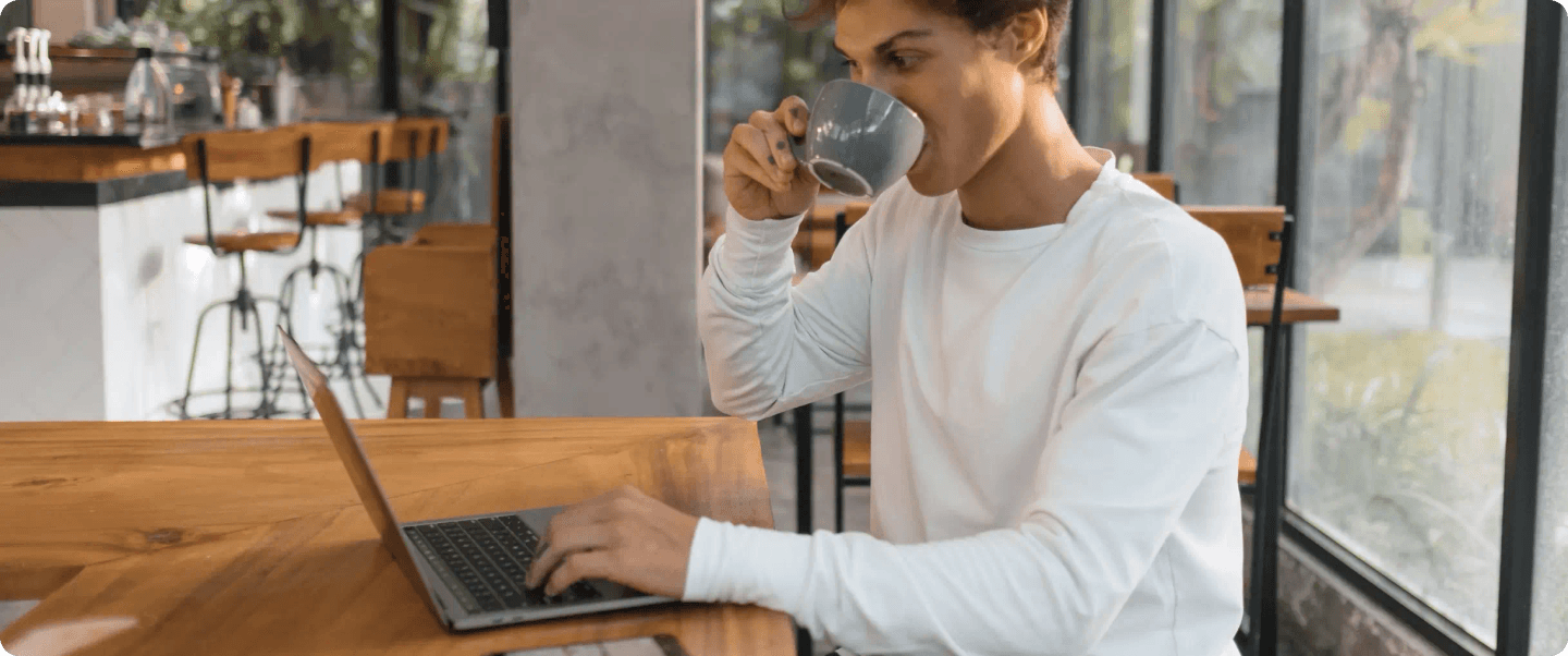 Person typing on a laptop while sipping coffee, creating an engaging email newsletter.
