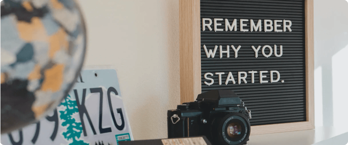An inspirational message that reads, REMEMBER WHY YOU STARTED, along with a globe and camera in the foreground.