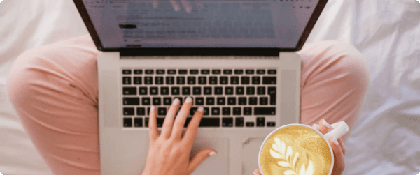 A woman typing an email sign-off on a laptop while holding a cup of coffee.