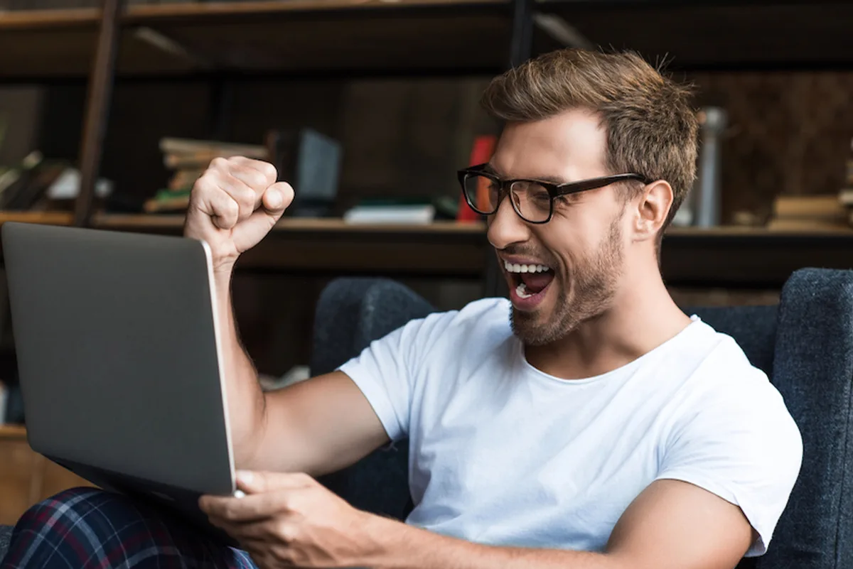 Young entrepreneur excitedly viewing successful email campaign results on his laptop, celebrating customer engagement.