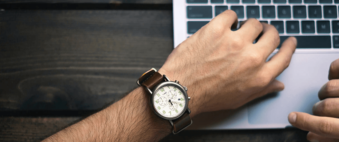 Close-up of a man's watch while he types on a laptop, representing the concept of time taken to build a startup.