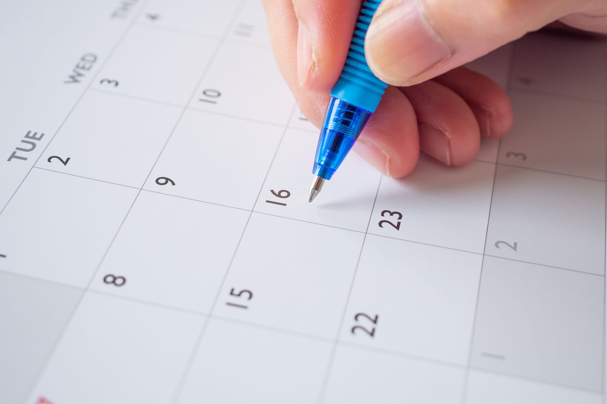 A hand holds a pen over a paper calendar, illustrating the simplicity of planning a newsletter with a basic editorial calendar.