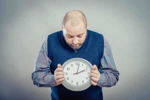 A man in a sweater vest looks down at a clock he’s holding, symbolizing the importance of choosing the best time to send marketing emails.