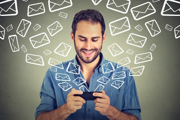 A person typing on their phone surrounding by floating email logos.