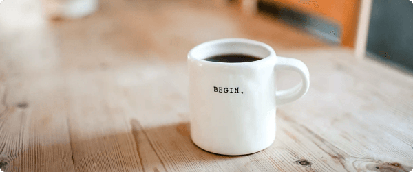 A coffee mug on a wooden table with the word BEGIN printed on the side.