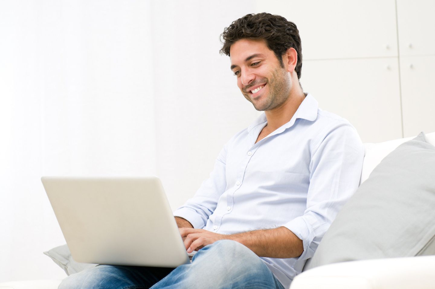 A smiling man using his laptop to create a newsletter campaign while sitting on the couch.