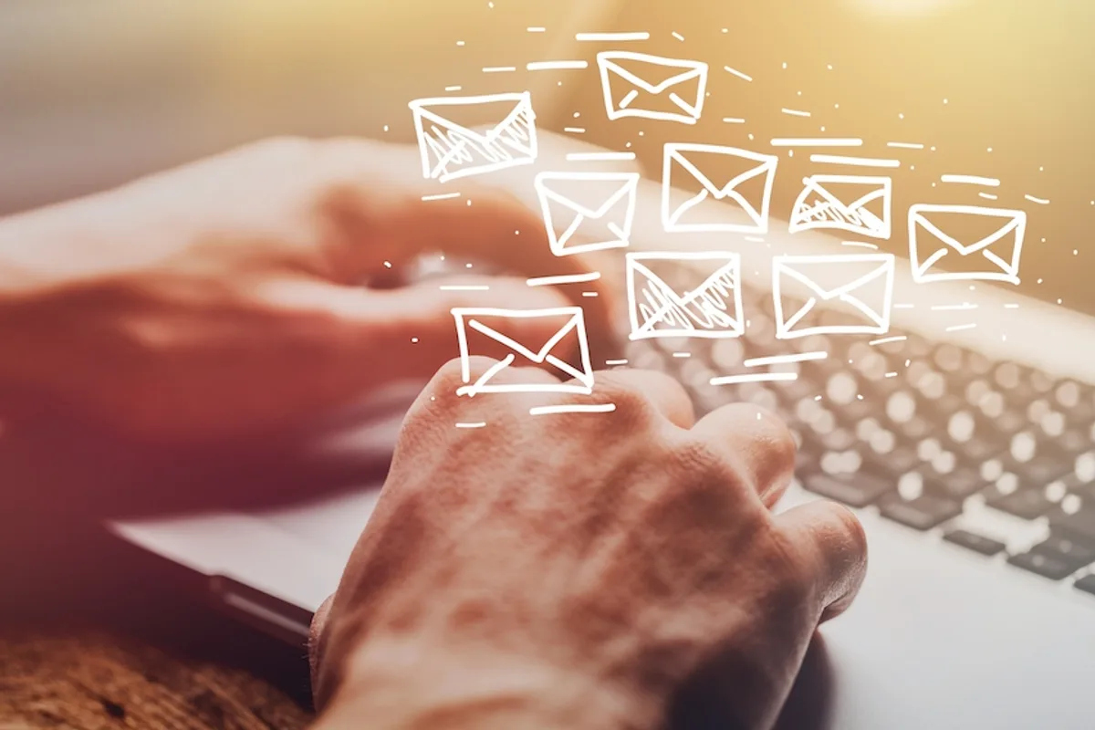 Hands on a notebook keyboard with floating email icons, depicting efficient use of bulk email marketing software.