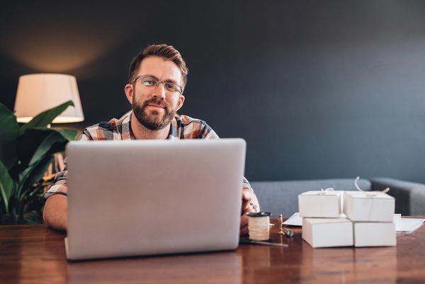 A bearded man working on a laptop in his cozy home office.