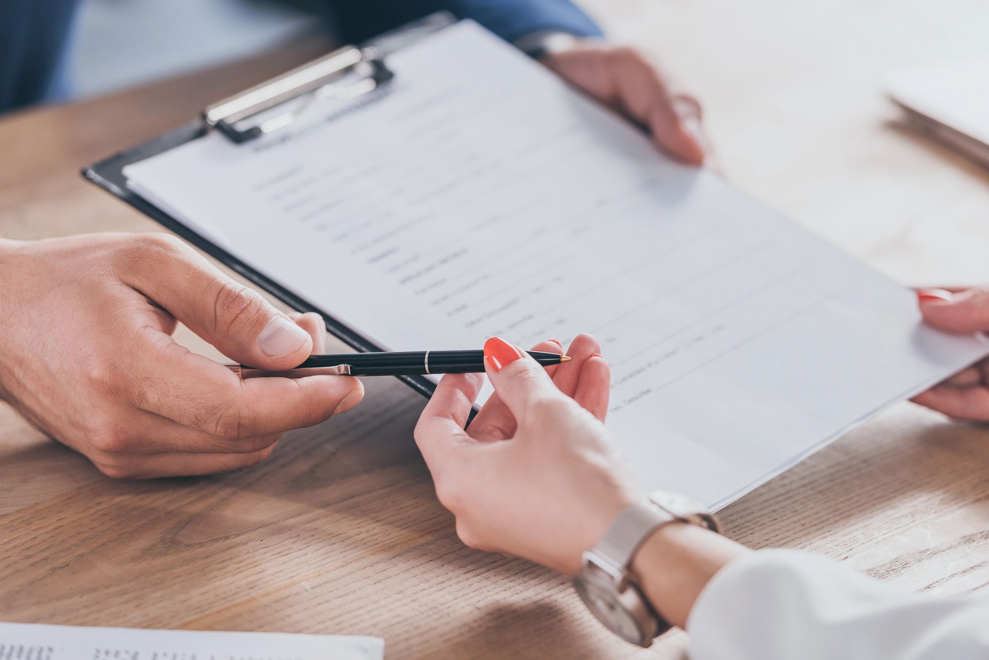 Passing a pen to sign a consent form on clipboard, symbolizing double‑opt‑in permission for building an email list.